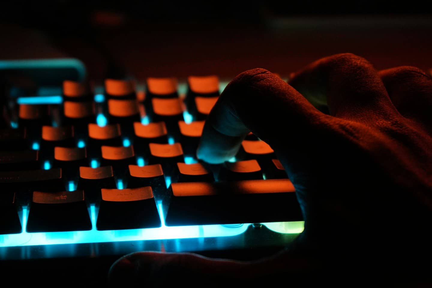 Hand typing on a glowing blue and cyan mechanical keyboard.