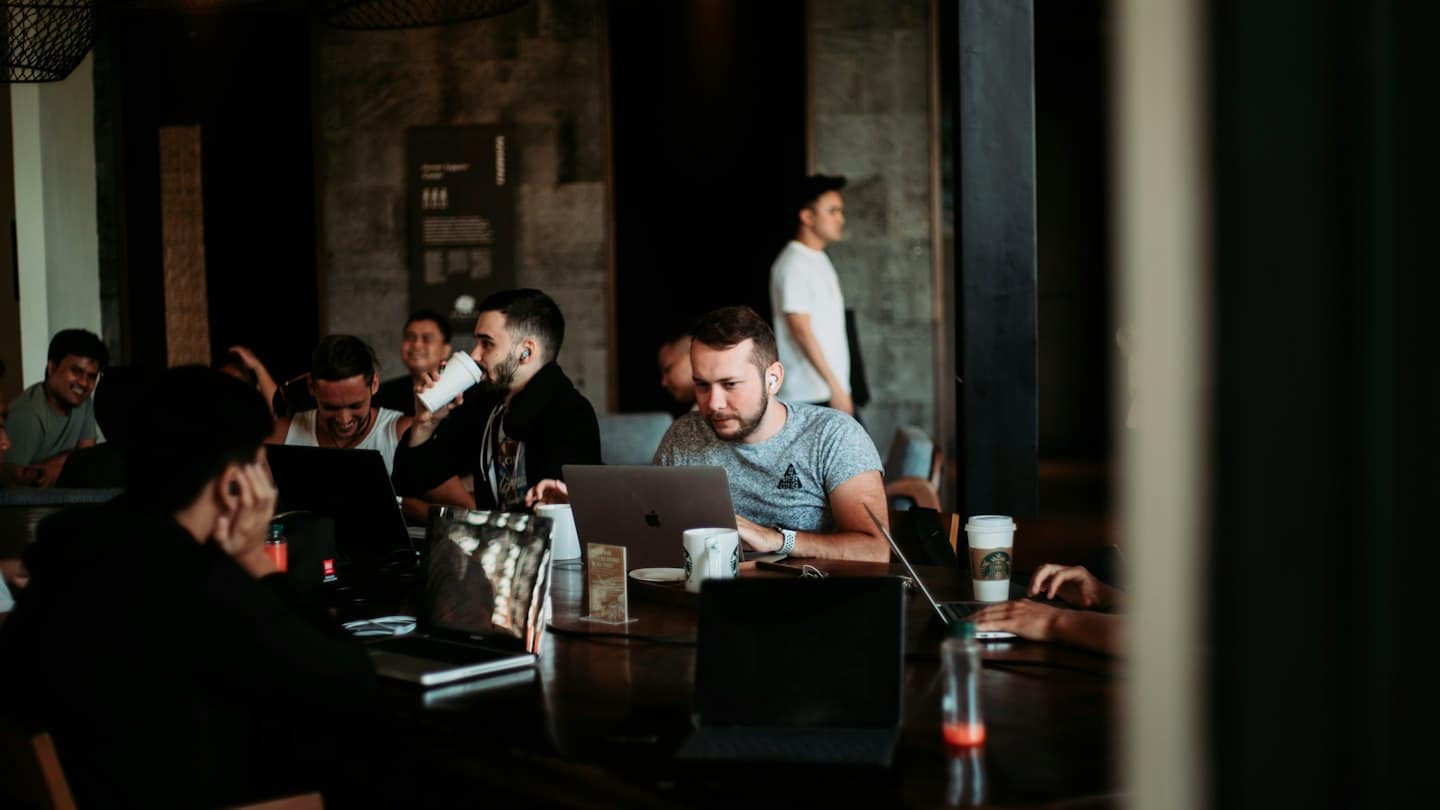 Young men collaborating on laptops at a cafe table.