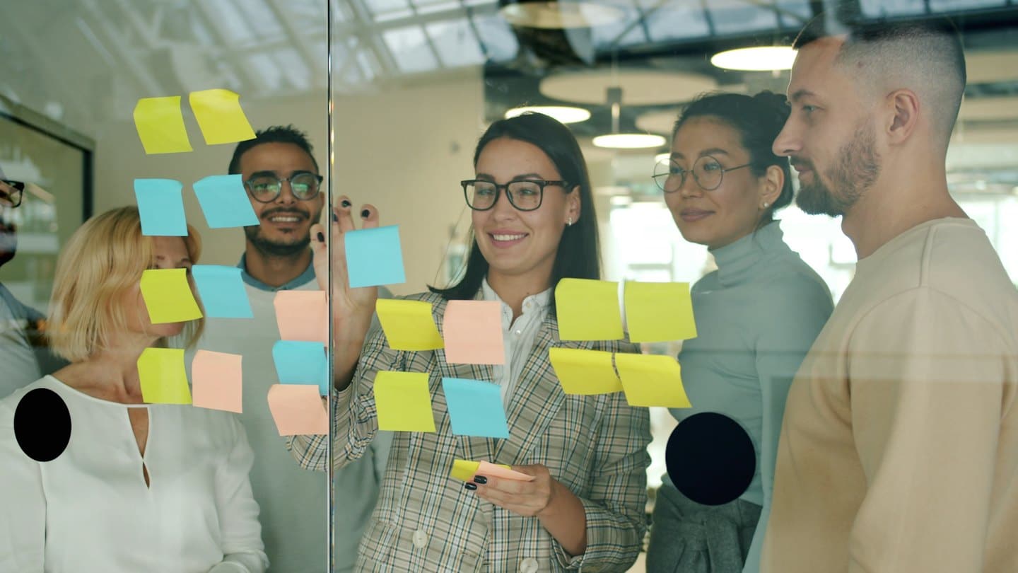 Diverse team brainstorming with sticky notes on glass board.
